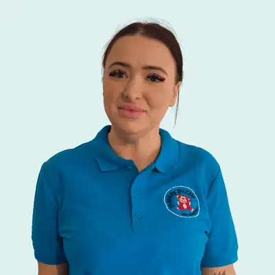 Bright young female nursery staff member wearing Monkey Puzzle Day Nursery & Preschool Lightwater uniform with logo, smiling for a welcoming photo.